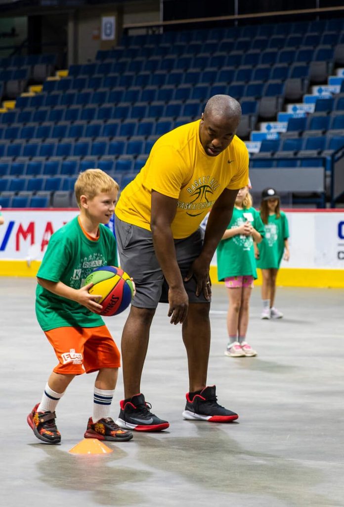 Kids Camp participant being coached while playing basketball at the Brandt Centre