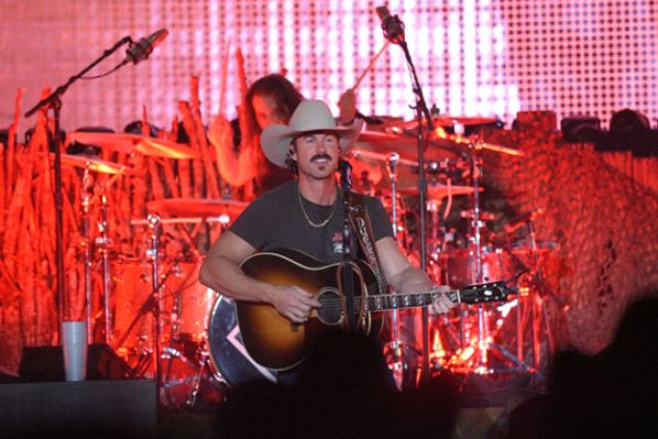 Musician performing on stage with guitar and drums.