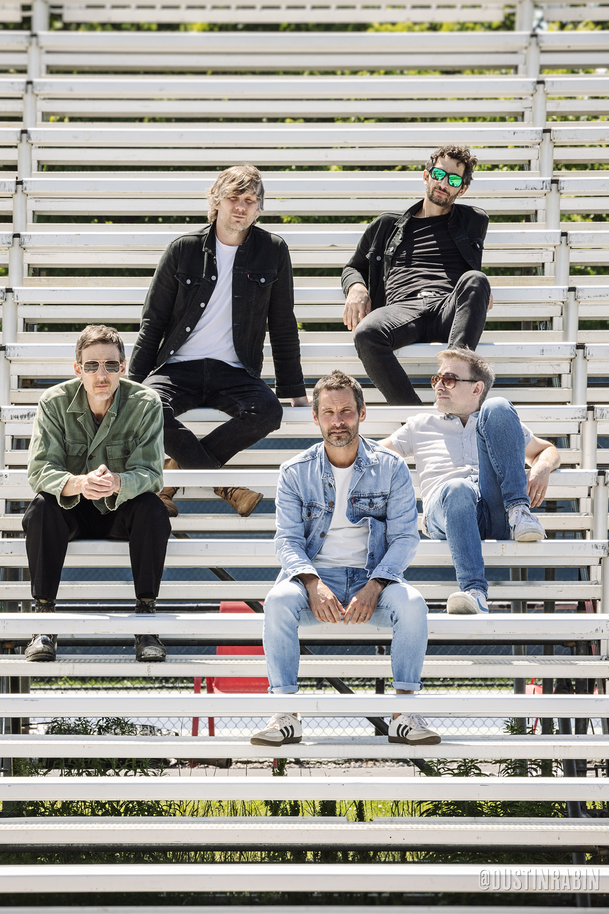 Group of five men sitting on bleachers.