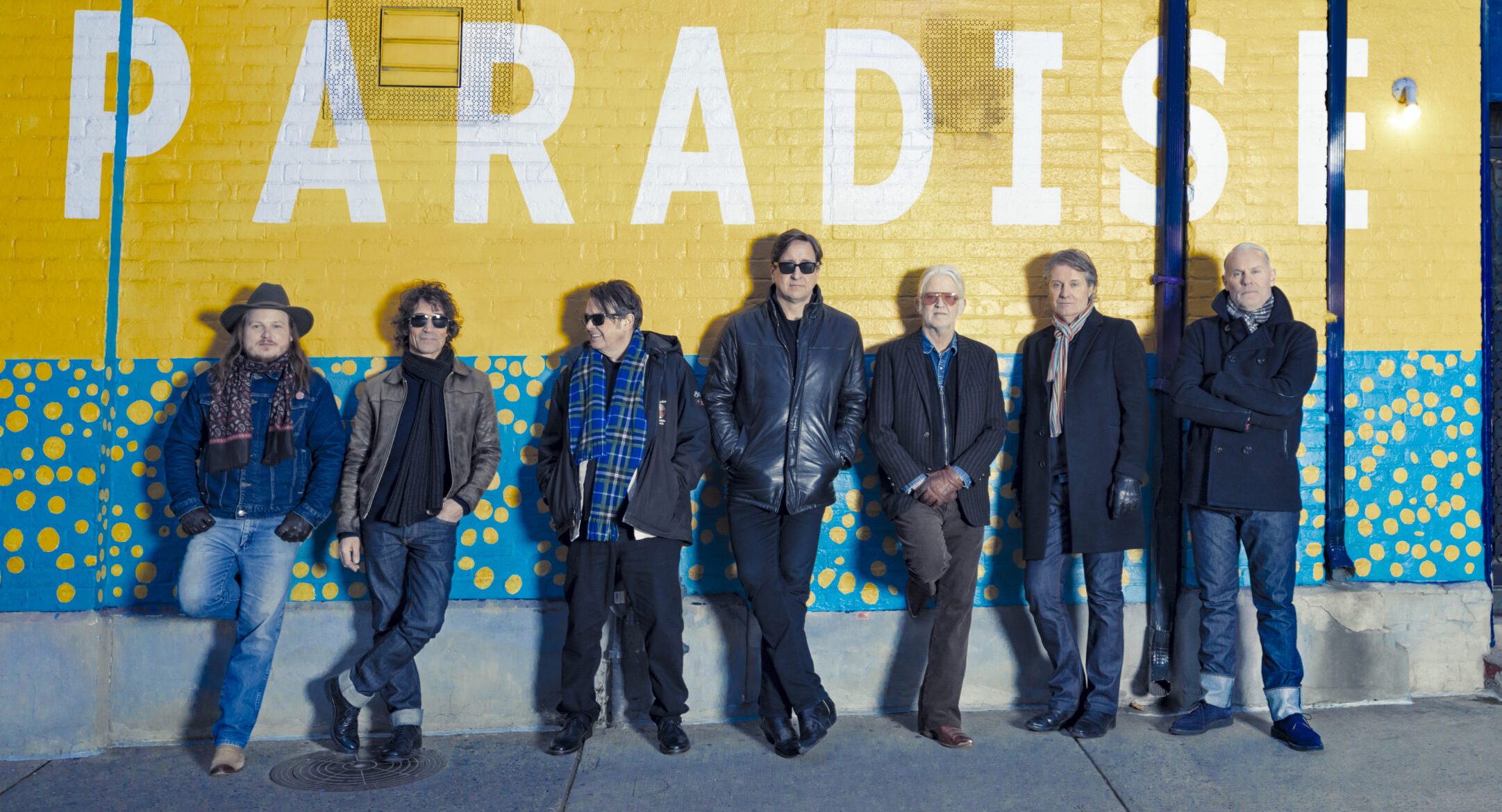 Blue Rodeo band members standing against Paradise wall.