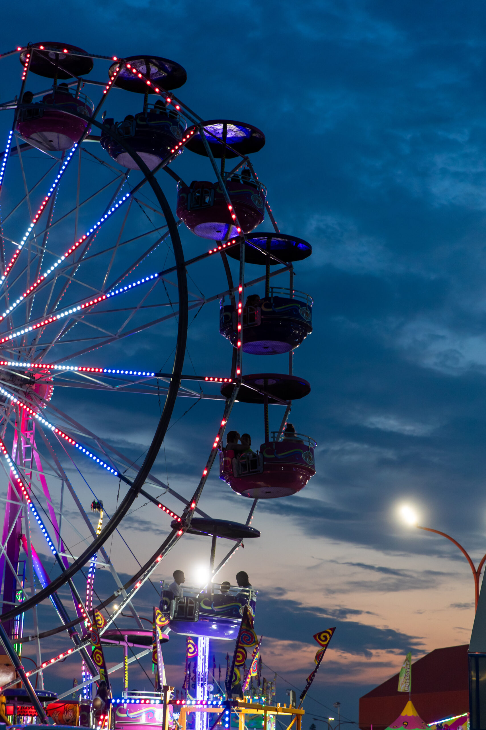 Illuminated Ferris wheel against evening sky at carnival.